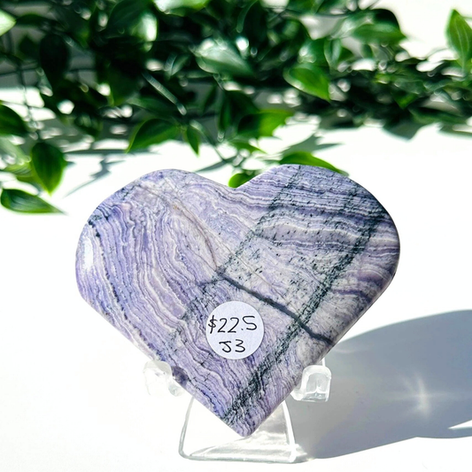Purple fluorite and white chalcedony crystal heart on stand with a white leafy background