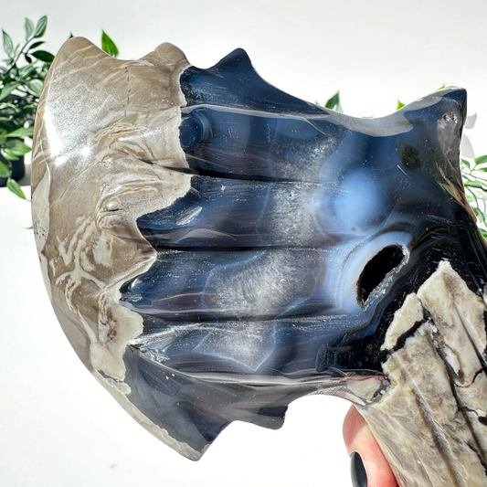 Hand holding a volcanic agate crystal axe with a natural pattern against a blurred green plant background