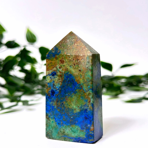 Azurite malachite crystal tower on a white and leafy background.