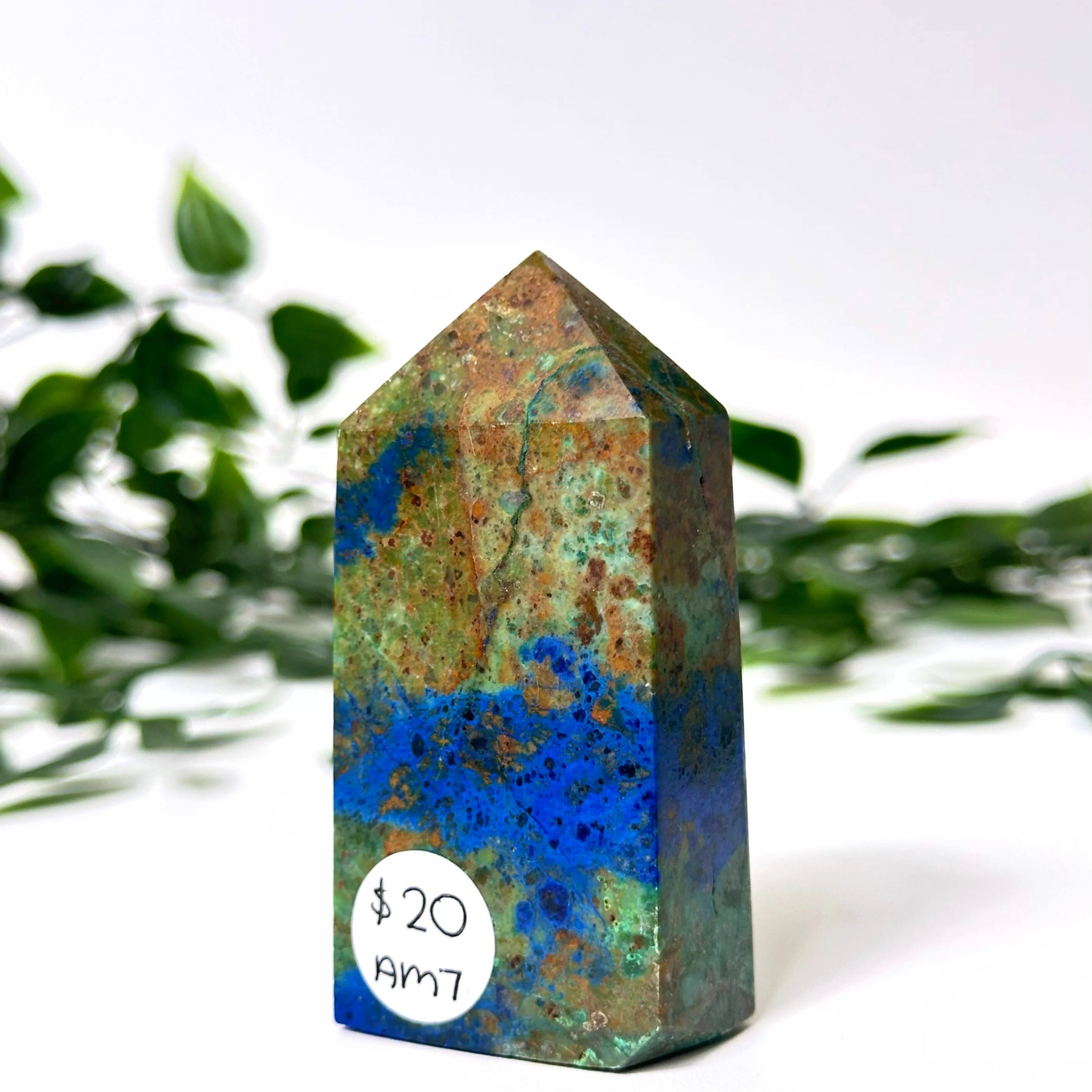 Azurite malachite crystal tower on a white and leafy background.