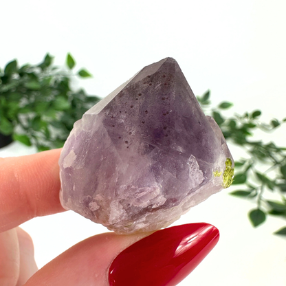 Amethyst point with epidote and hematite inclusions on a white background