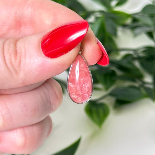 Rhodochrosite gemstone pendant held against a green leafy background