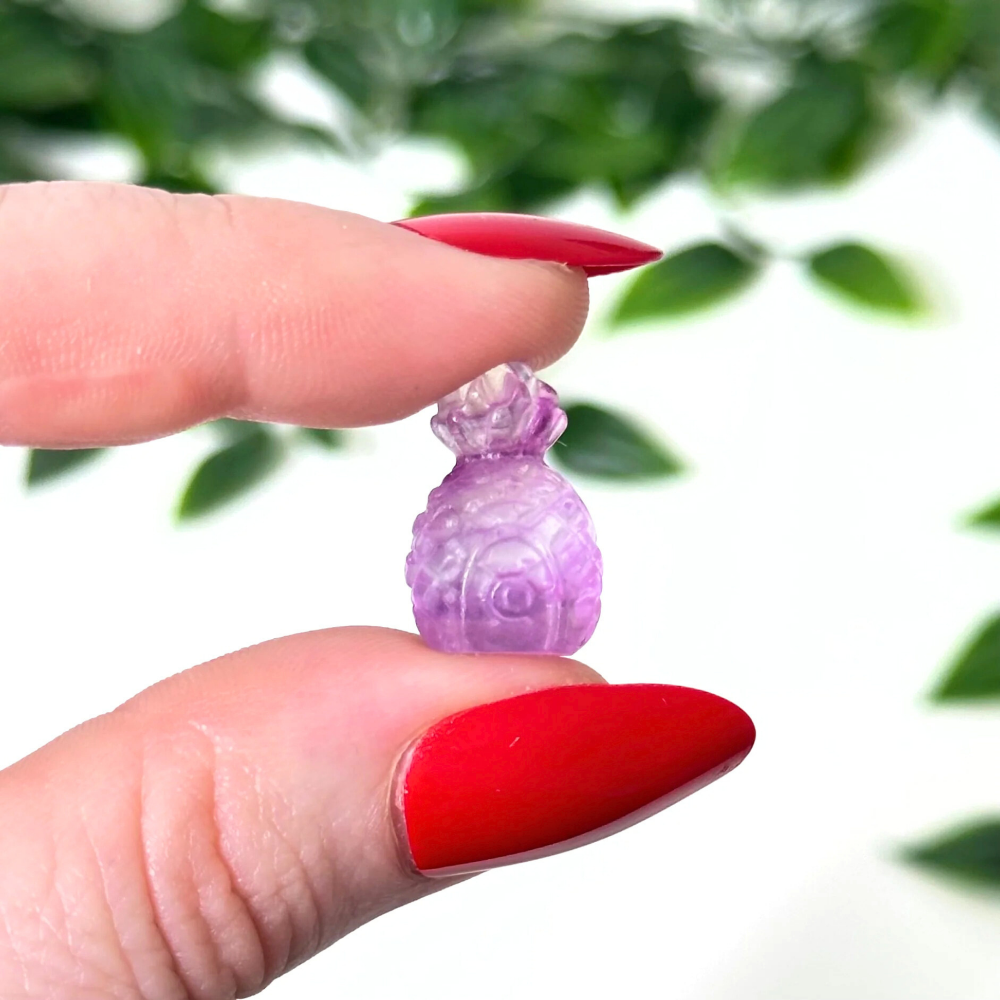 Hand holding a mini fluorite crystal carving on a white background
