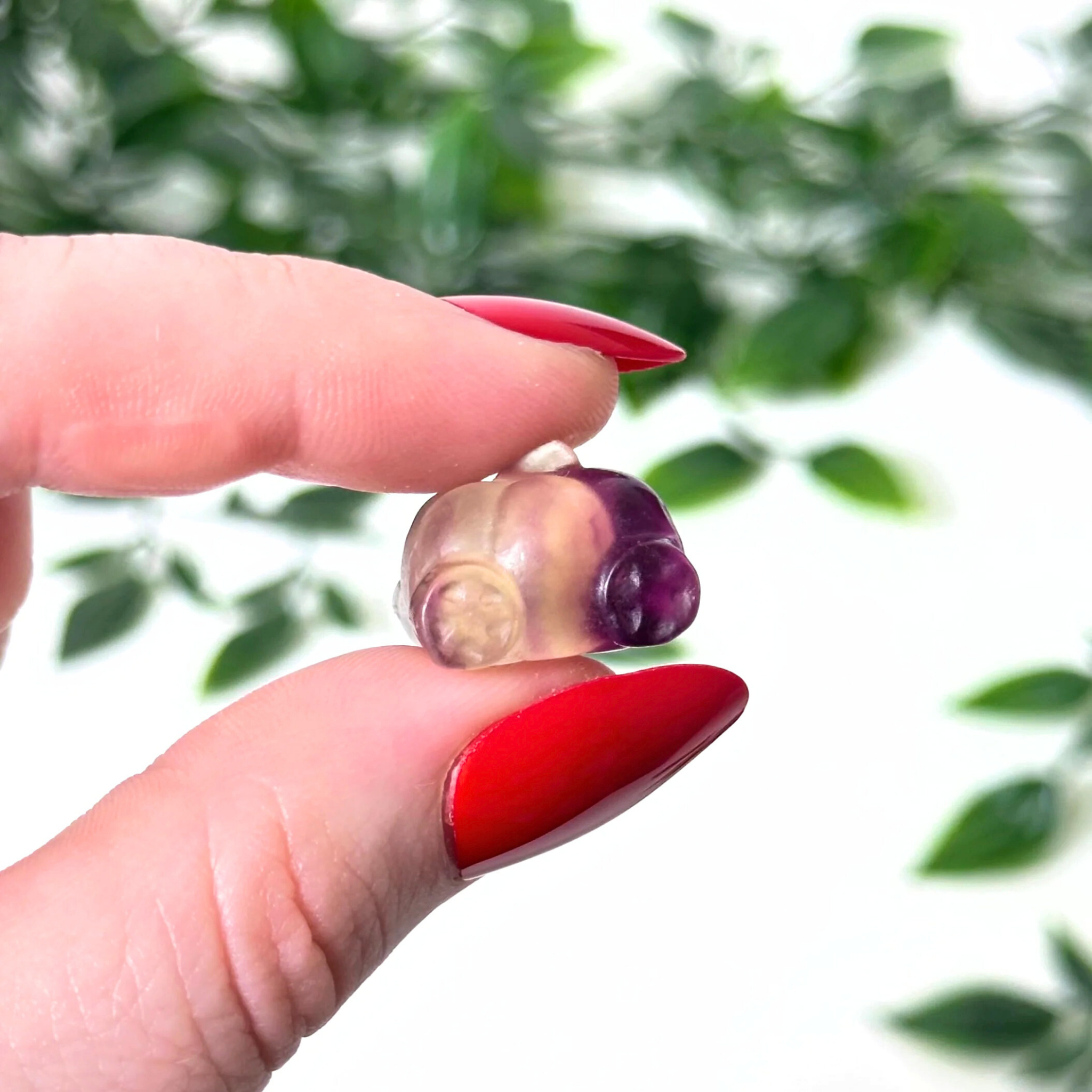 Hand holding a mini fluorite crystal carving on a white background
