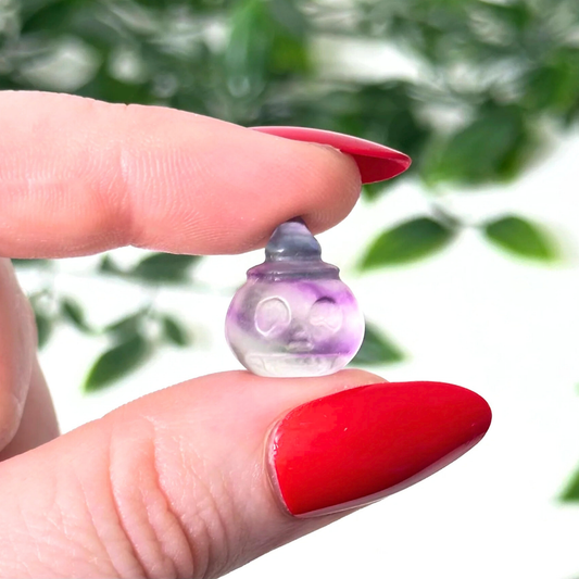 Hand holding a mini fluorite crystal carving on a white background