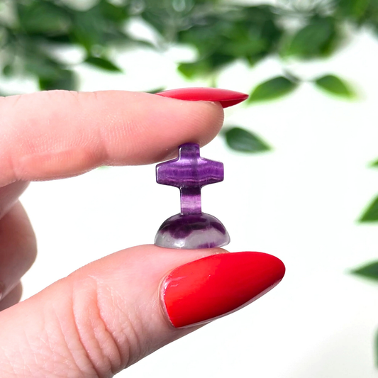Hand holding a mini fluorite crystal carving on a white background