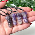 Hand holding three amethyst necklaces with a blurred green background