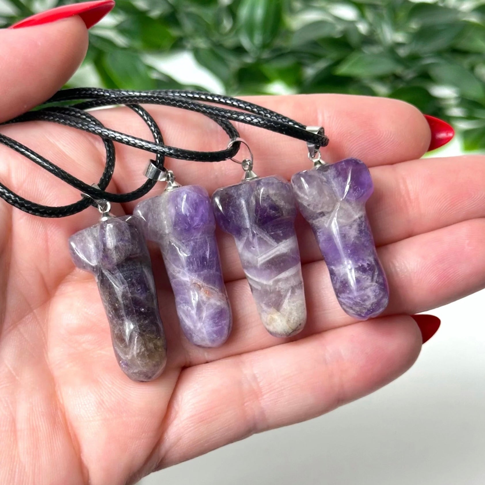 Hand holding three amethyst necklaces with a blurred green background