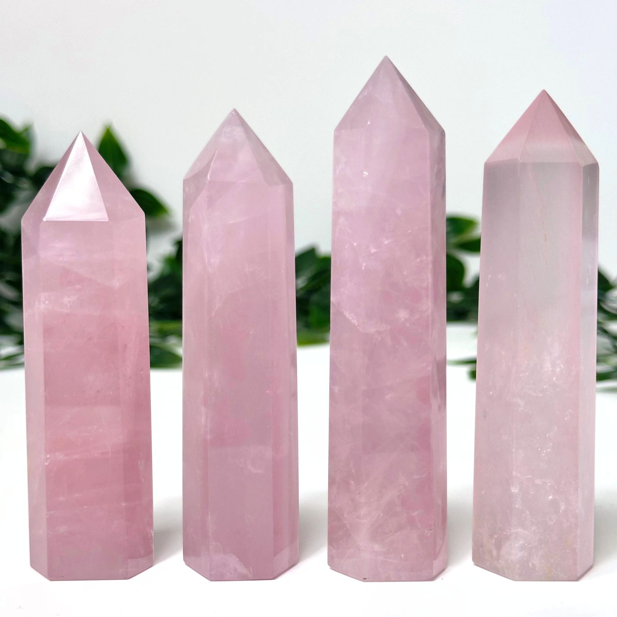 4 rose quartz crystal towers in front of a white and leafy background