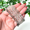 Hand holding a stack of himalayan quartz bracelets on a white leafy background