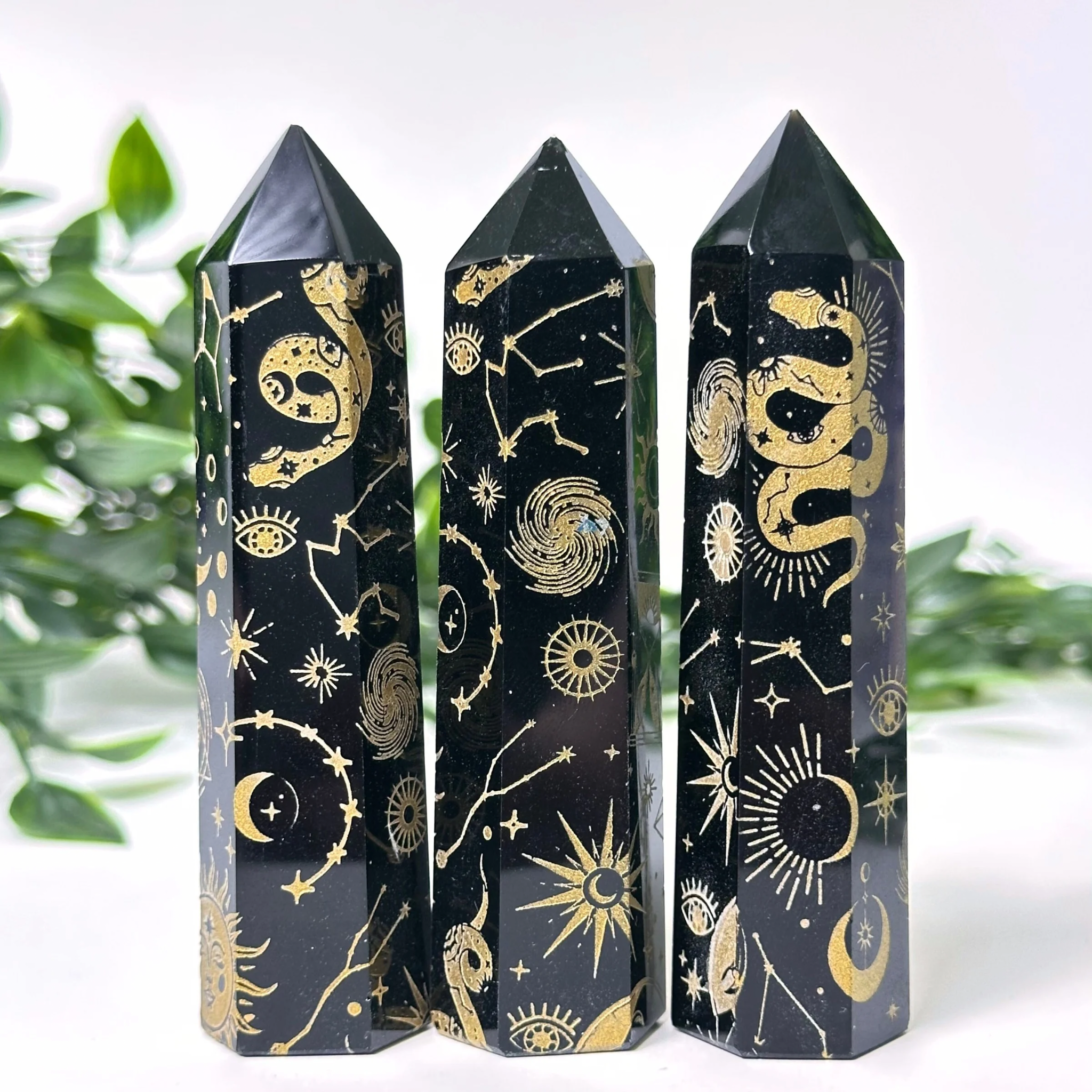 Three Black Obsidian crystal towers with gold astrological symbols on a white background