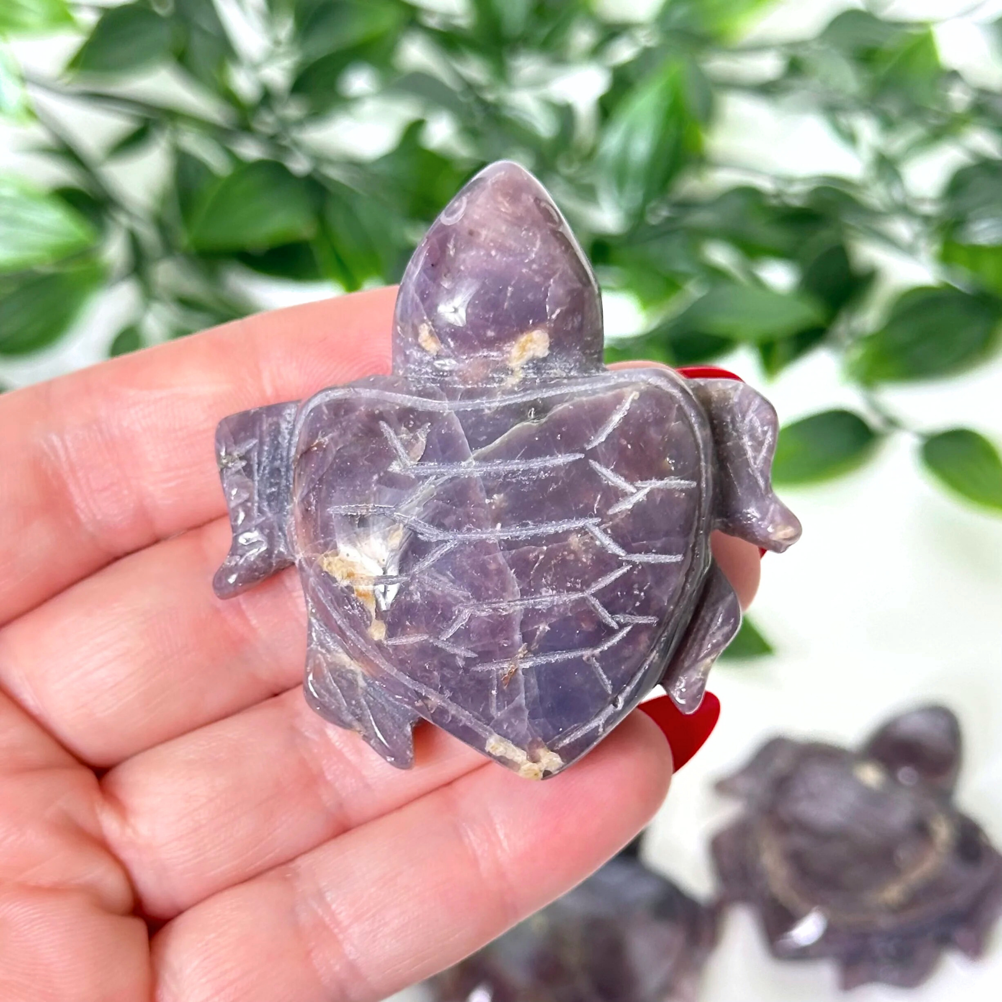 Hand holding a purple rose quartz turtle crystal carving against a blurred background.