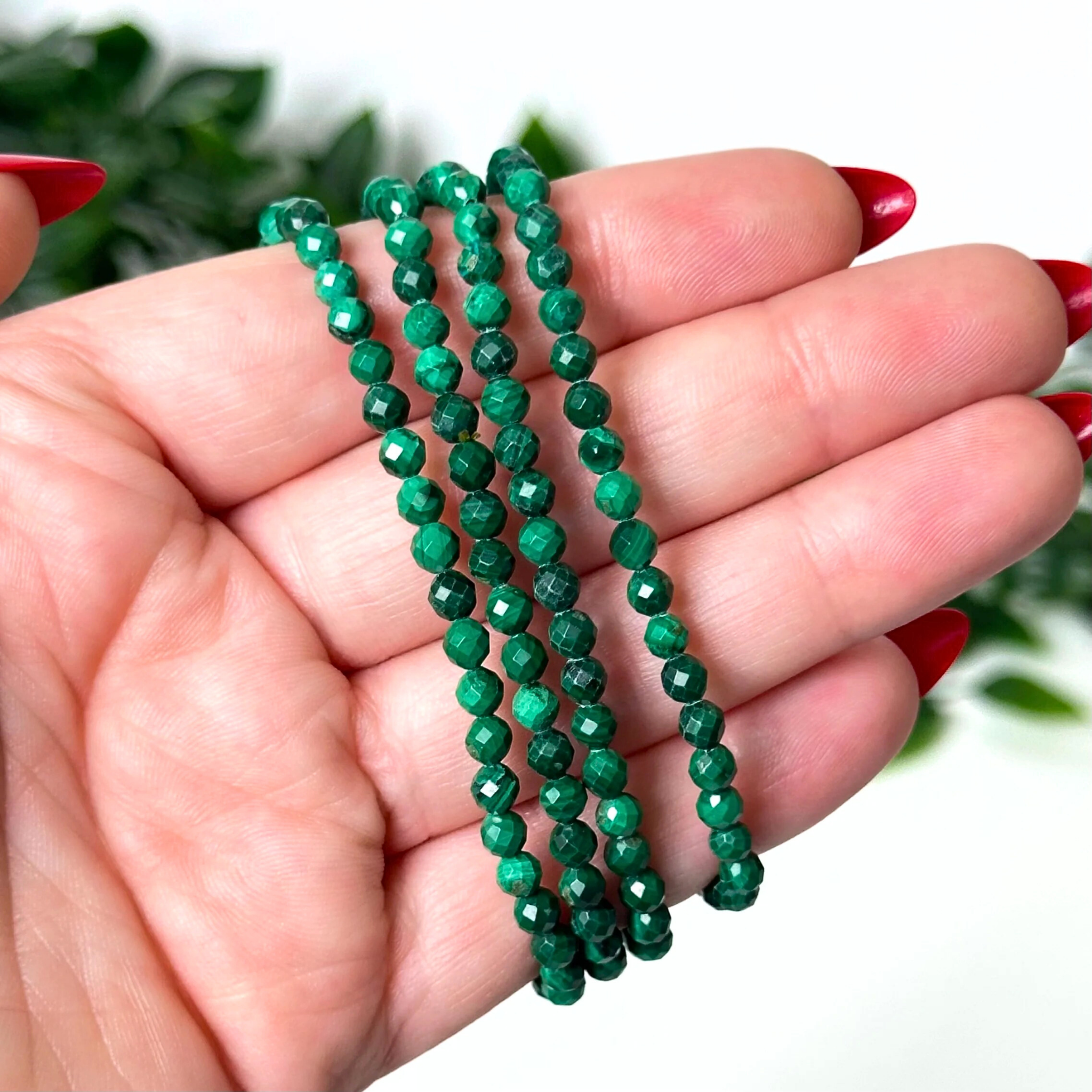 Hand holding green Malachite crystal bracelets against a white background.