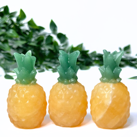 3 orange calcite pineapple crystal carvings on a white leafy background