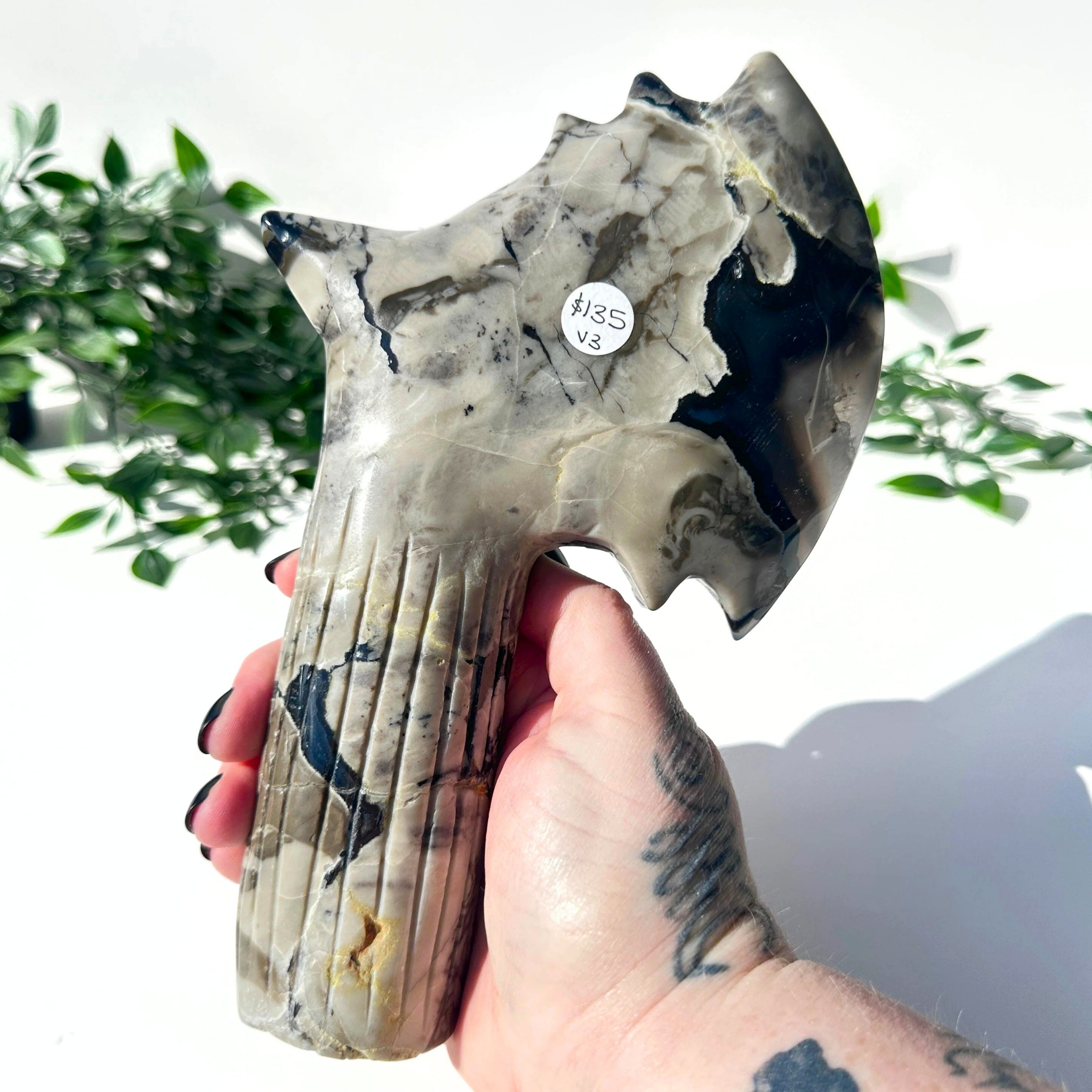 Hand holding a large agate crystal axe with a blurred green plant background