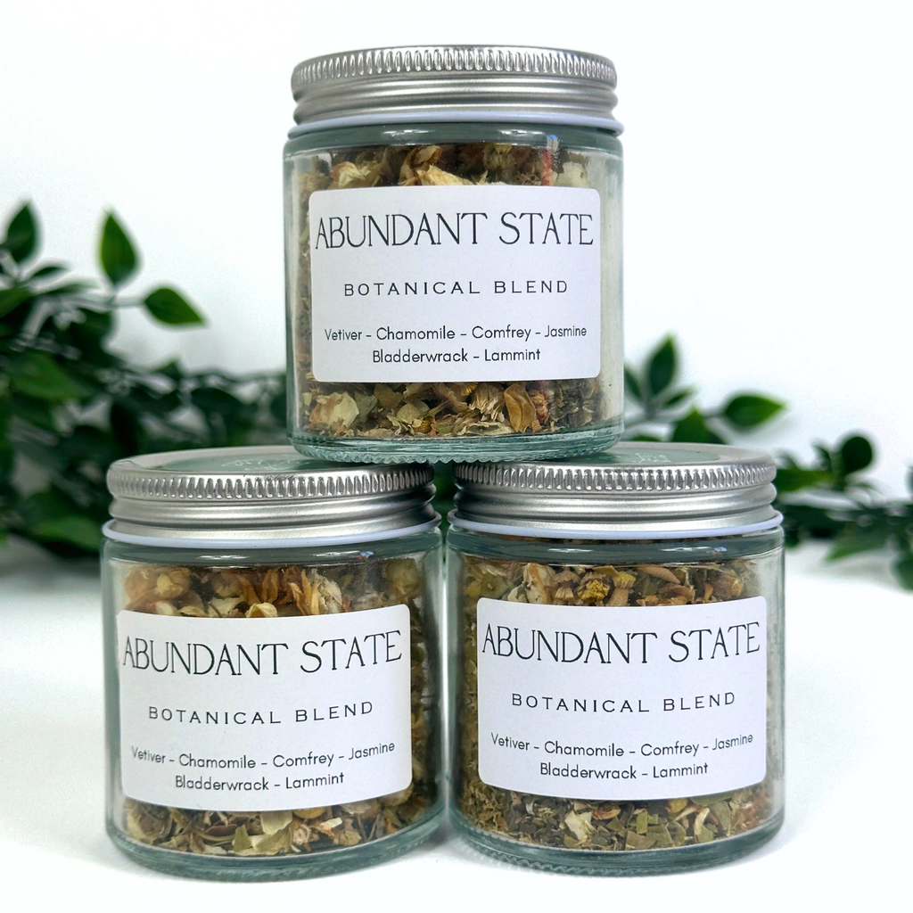 Three jars of Abundant State Botanical Blend on a white background with greenery.