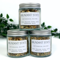 Three jars of Abundant State Botanical Blend on a white background with greenery.