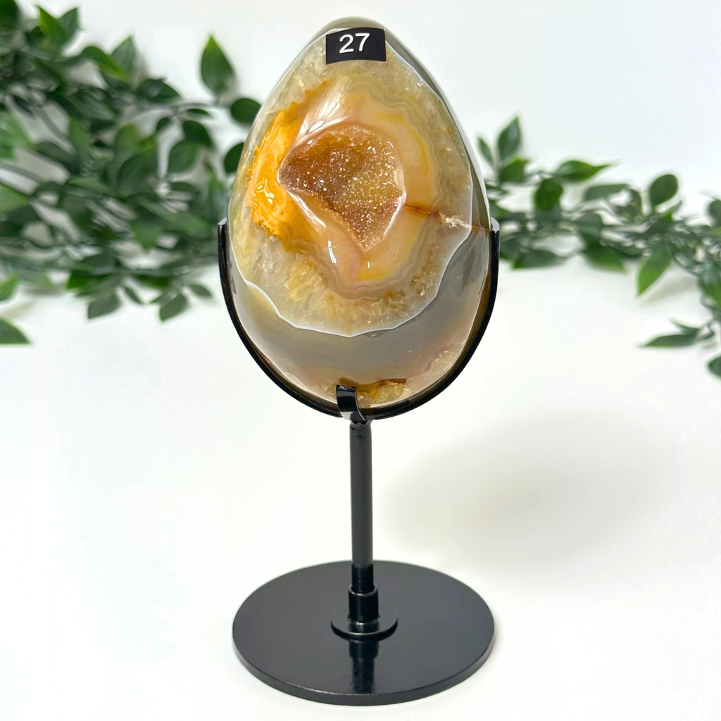 Druzy agate egg on a stand with green foliage in the background
