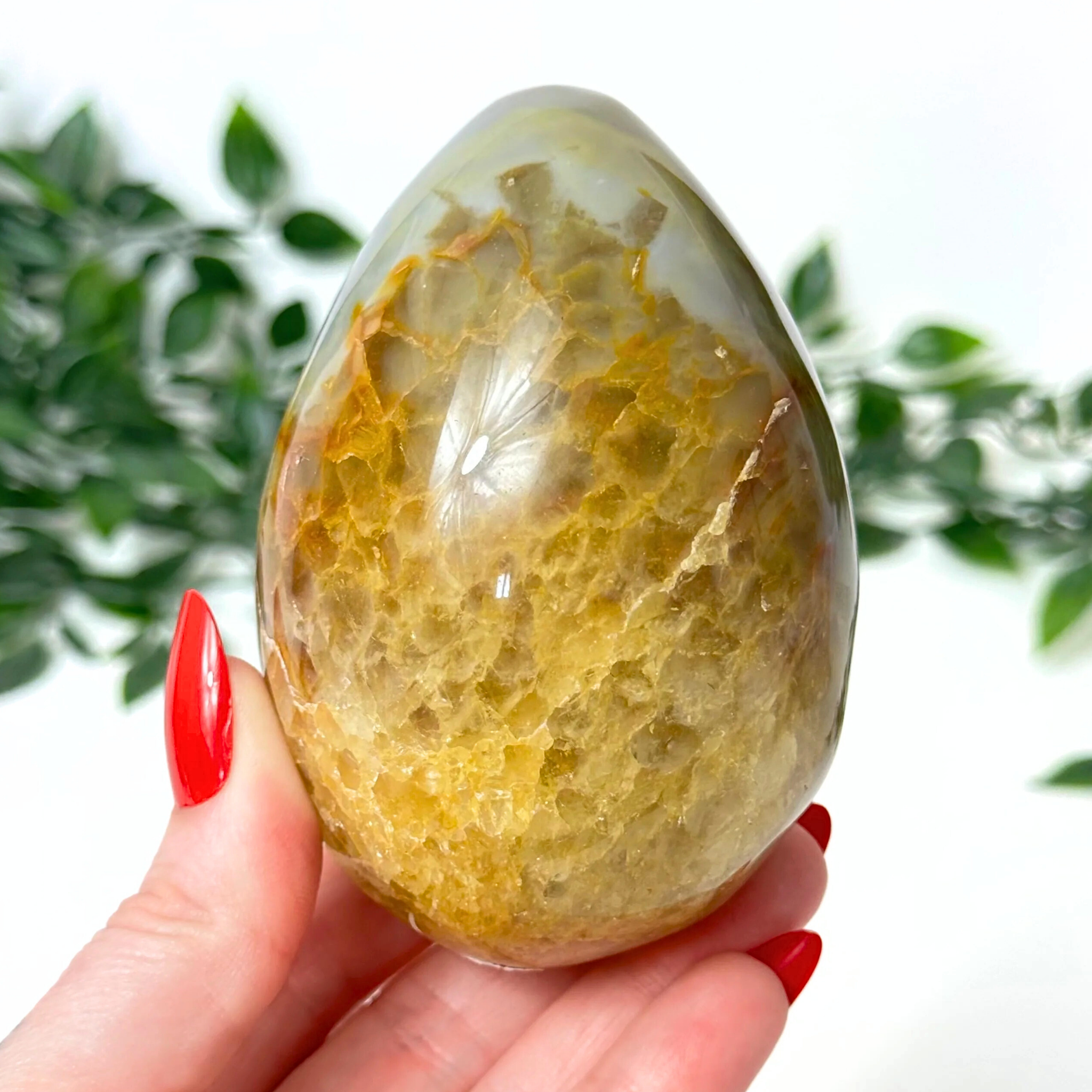 Hand holding a yellow druzy agate egg with a blurred green leafy background