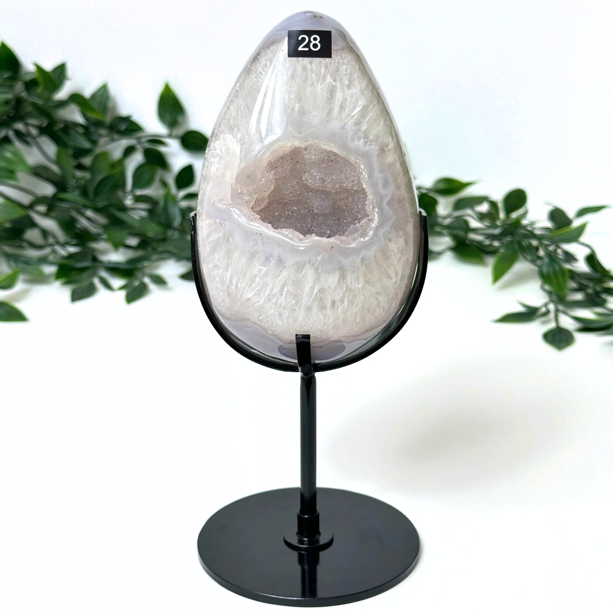 Druzy agate crystal egg on a stand with green foliage in the background