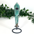 Teal amazonite crystal on a stand with greenery in the background