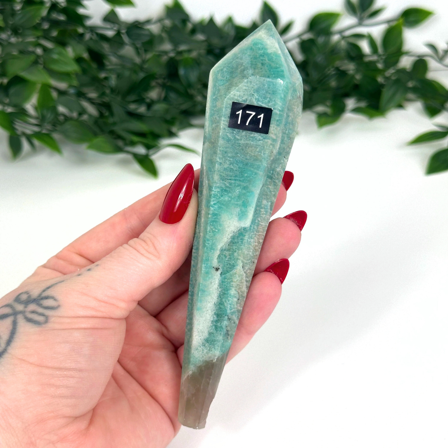 Hand holding an amazonite crystal against a white background with greenery