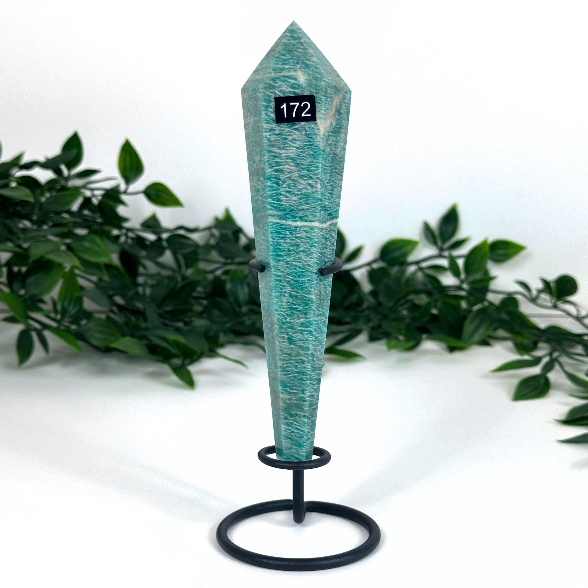 Teal amazonite crystal on a stand with greenery in the background