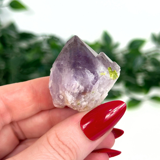Hand holding an amethyst crystal with a blurred green background