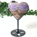 Heart shaped amethyst crystal on black stand on a white leafy background