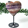 Heart-shaped amethyst stone on a stand with a white background and greenery