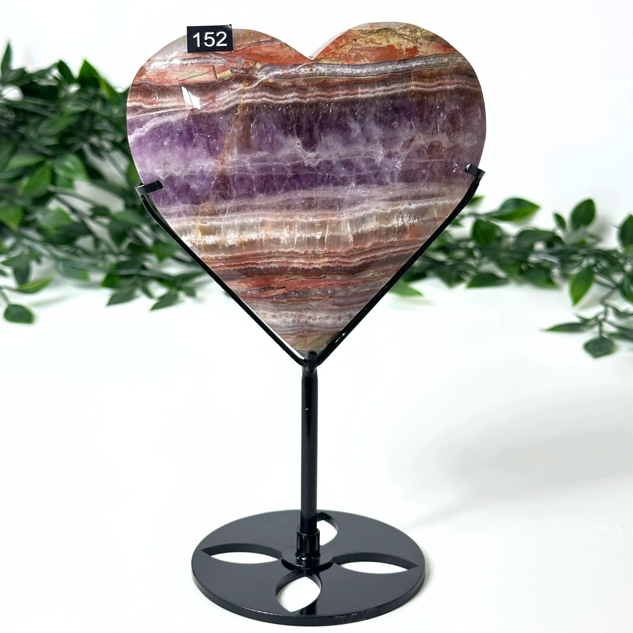 Heart-shaped amethyst stone on a stand with a white background and greenery