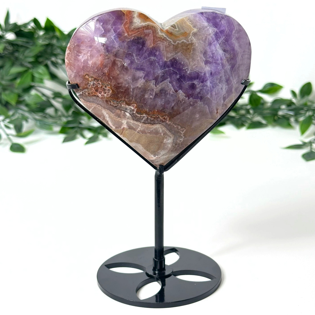Heart-shaped amethyst crystal on a stand with a green leafy background