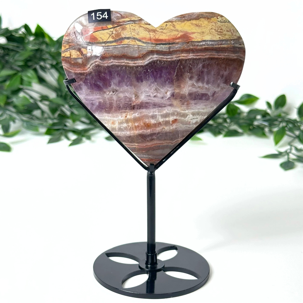 Heart-shaped amethyst stone on a stand with a green leafy background