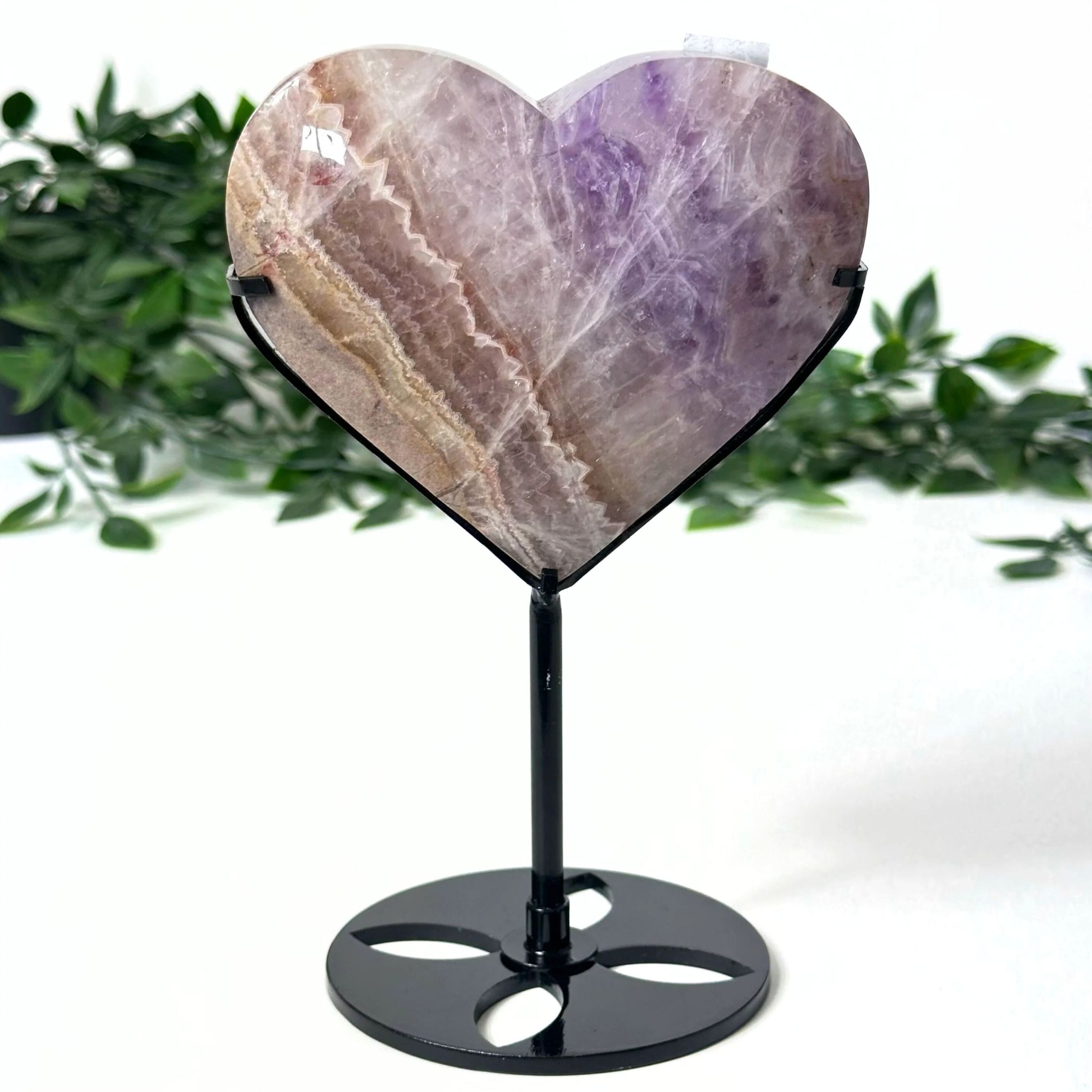 Heart-shaped amethyst crystal on a stand with a natural background