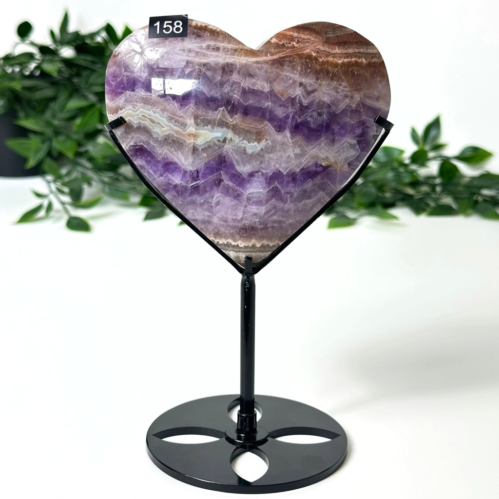 Heart-shaped amethyst crystal on a black stand with green foliage in the background