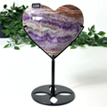 Heart-shaped amethyst crystal on a black stand with green foliage in the background