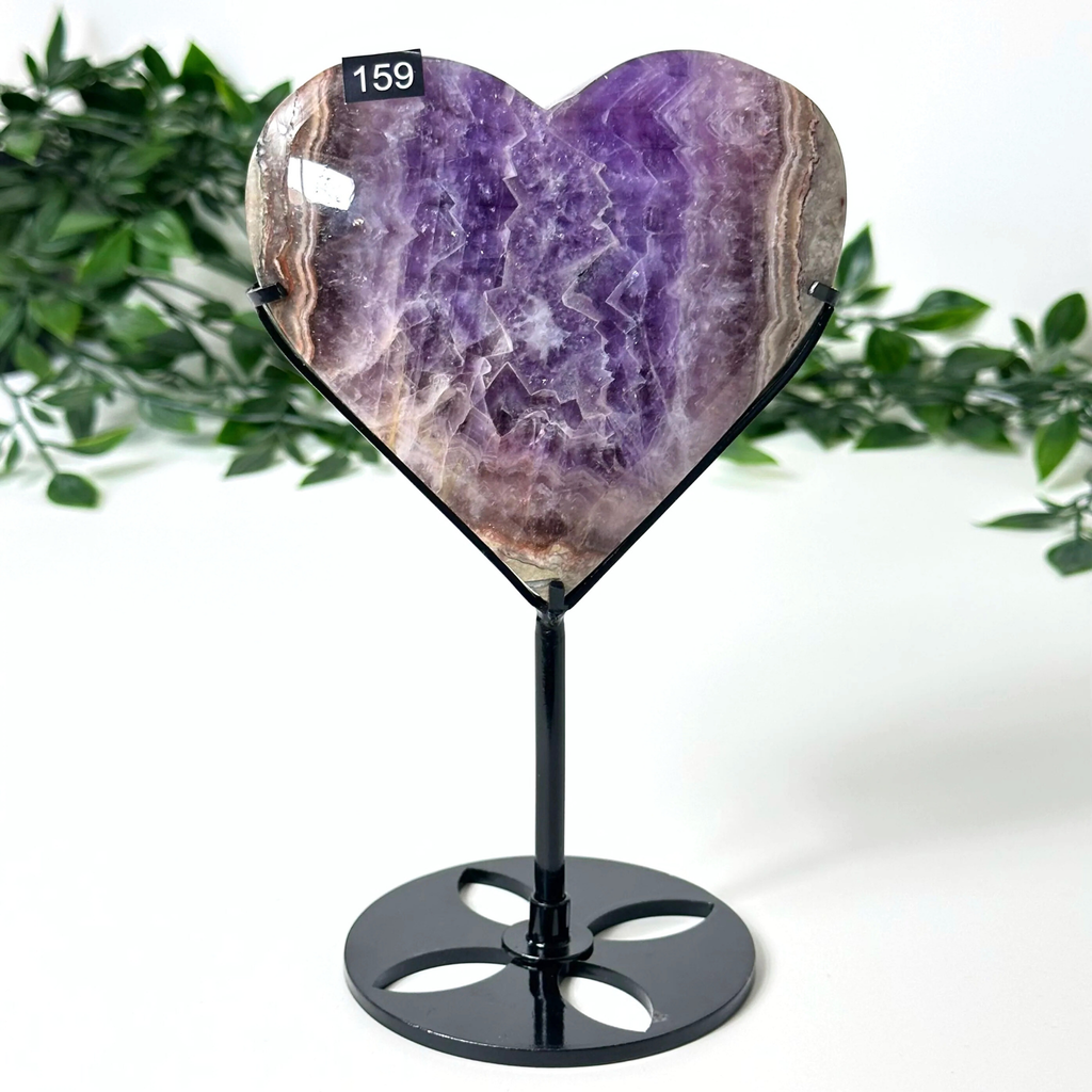Heart-shaped amethyst crystal on a black stand with green foliage in the background