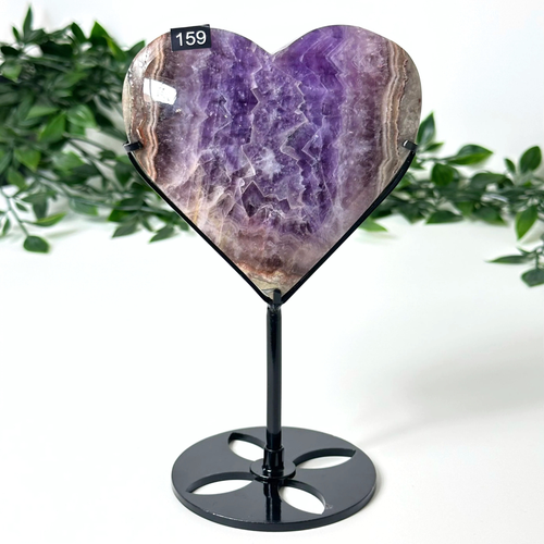 Heart-shaped amethyst crystal on a black stand with green foliage in the background