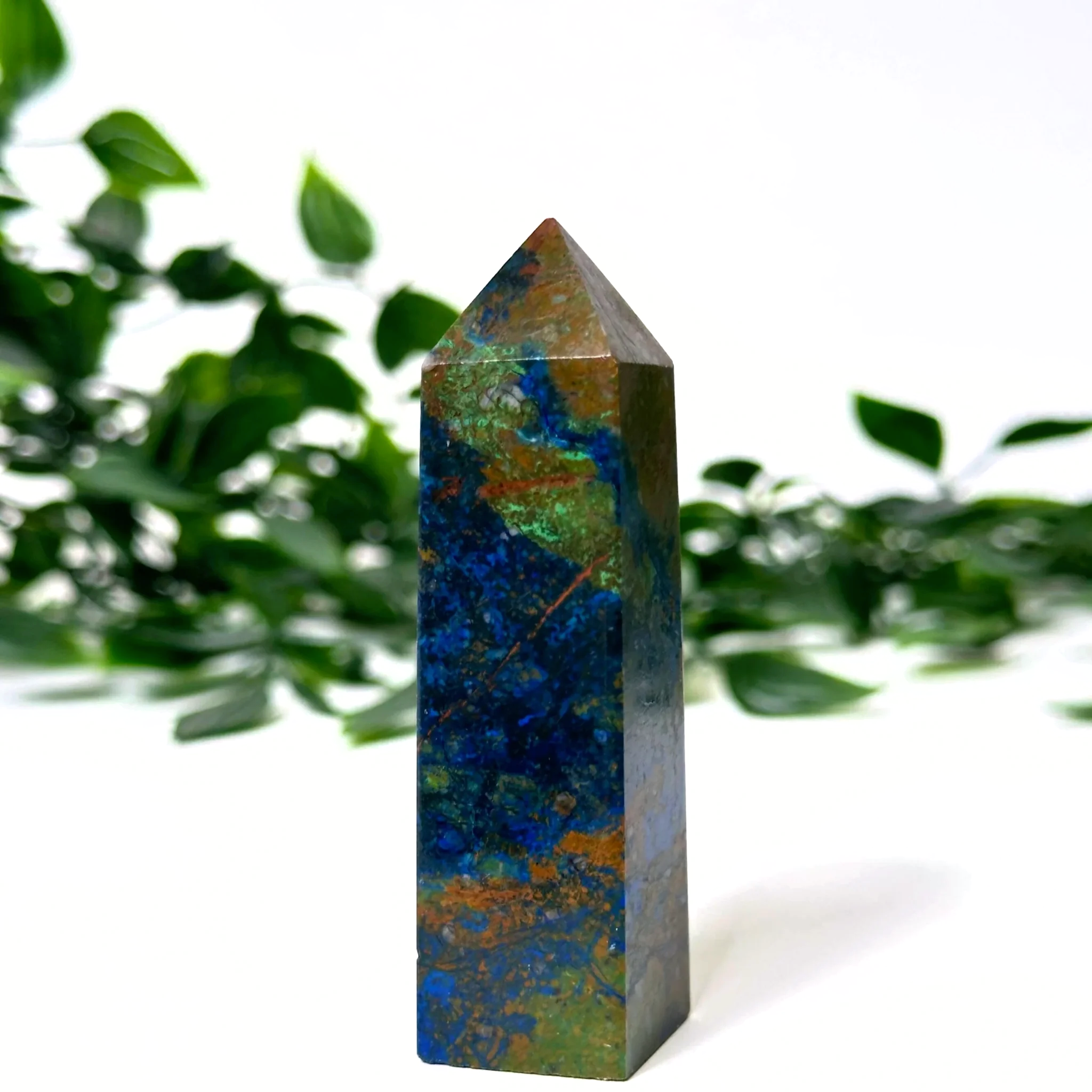 Azurite and malachite crystal tower with green leaves in the background