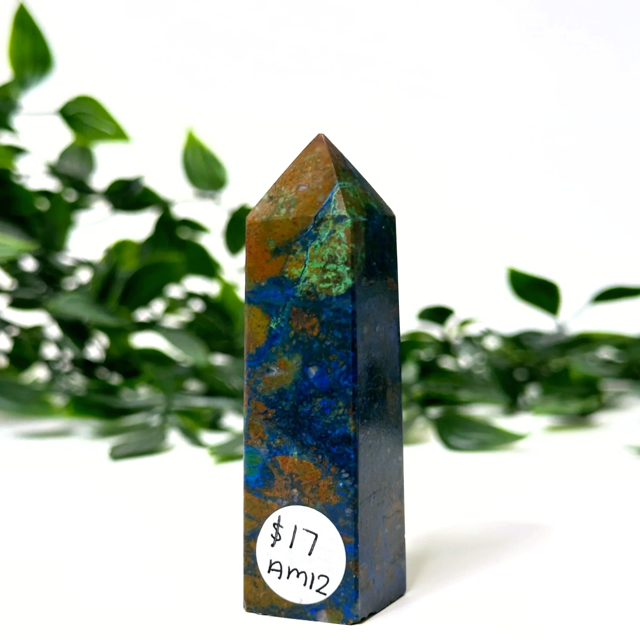Azurite and malachite crystal tower with a label in front of green foliage