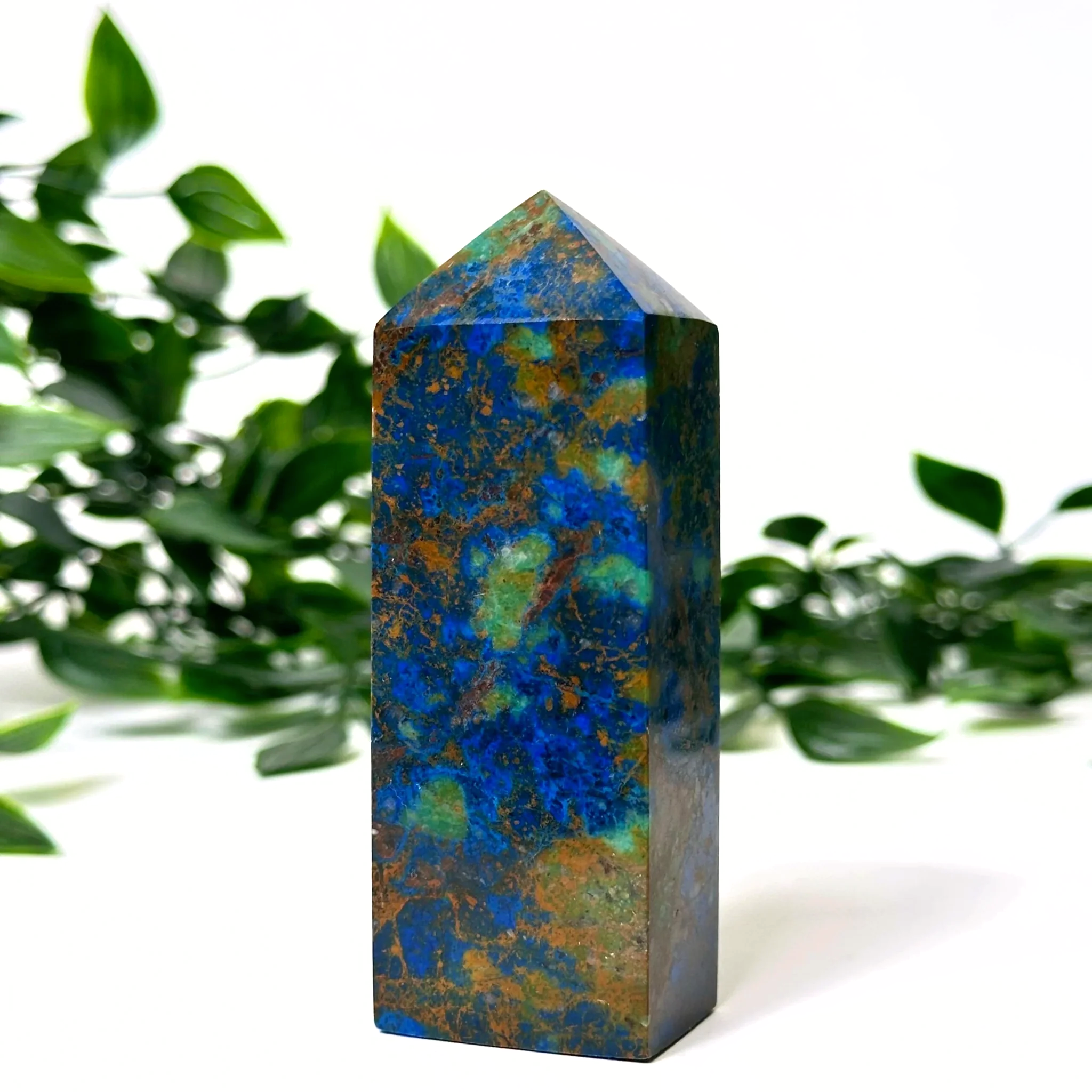 Azurite and malachite crystal tower with blue and green patterns against a blurred green leafy background