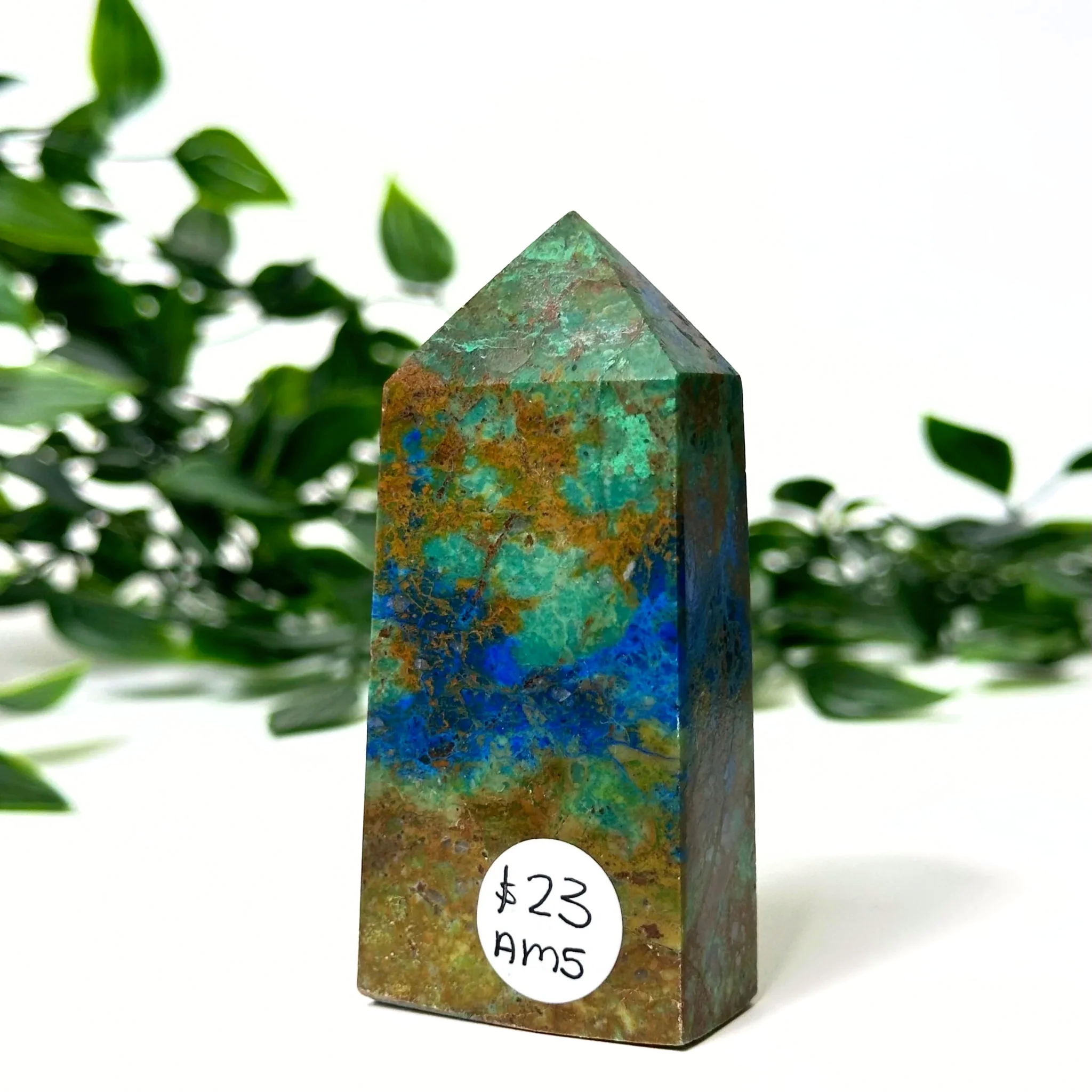 Azurite and malachite crystal tower with a label in front of green foliage