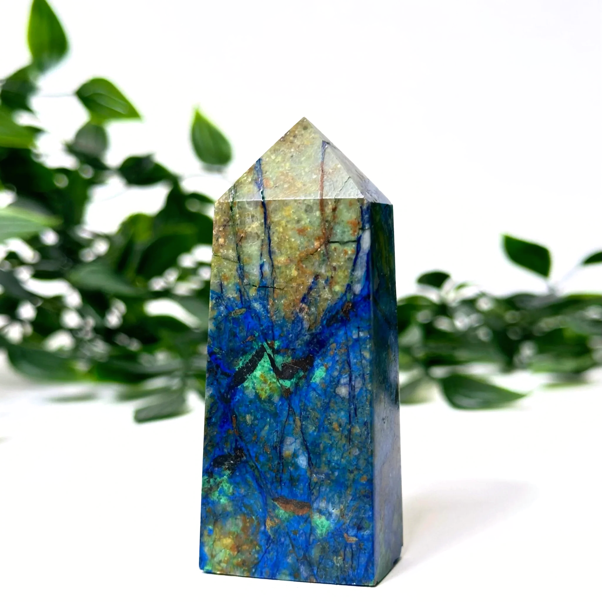 Azurite and malachite crystal tower with blue and green patterns against a blurred green leafy background