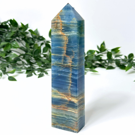 Blue onyx crystal tower with blue and gold patterns on a white background with green leaves.