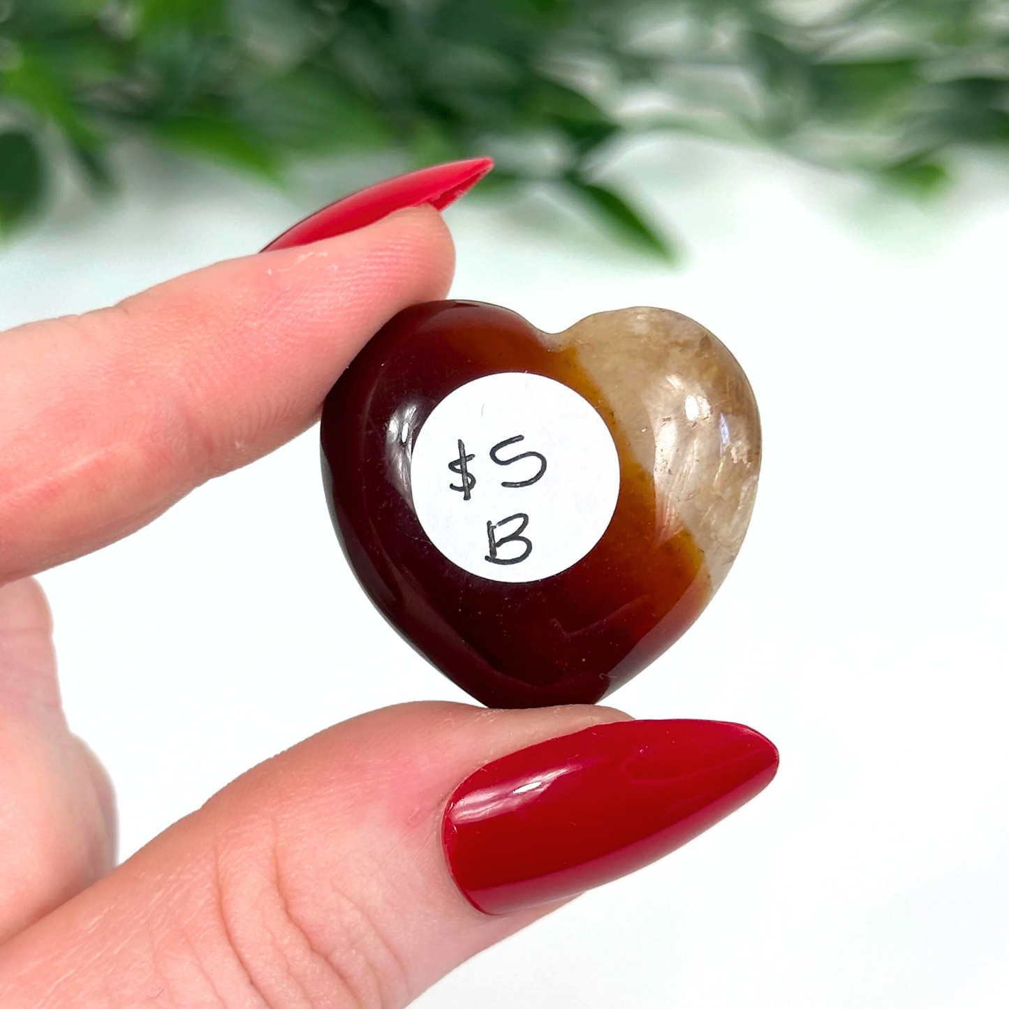 Heart-shaped carnelian crystal held by a hand against a blurred green background