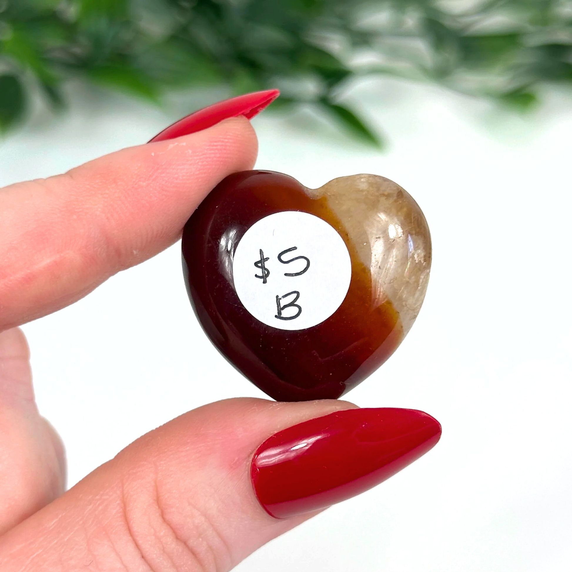 Heart-shaped carnelian crystal held by a hand against a blurred green background