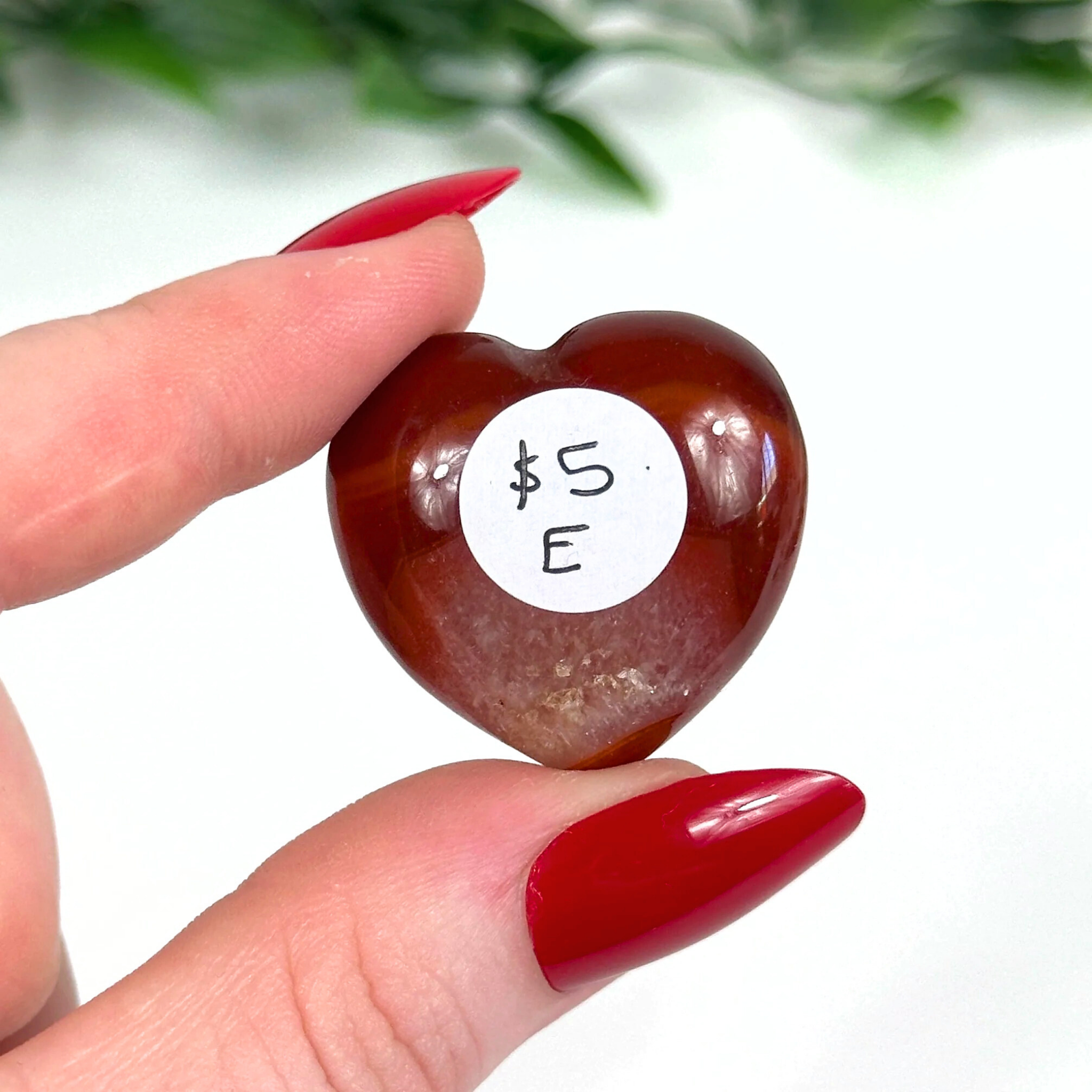 Heart-shaped carnelian crystal held by a hand with red nail polish.