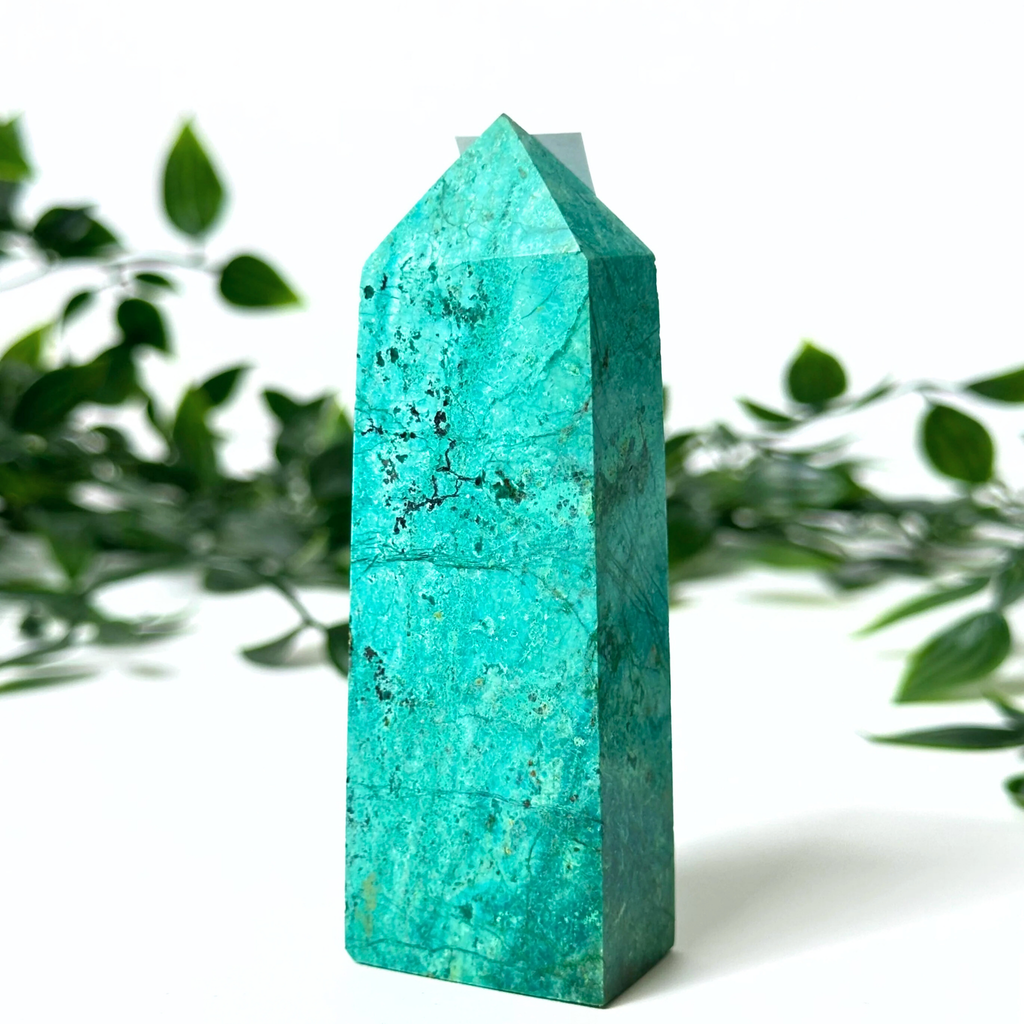 Chrysocolla crystal tower with green leaves in the background