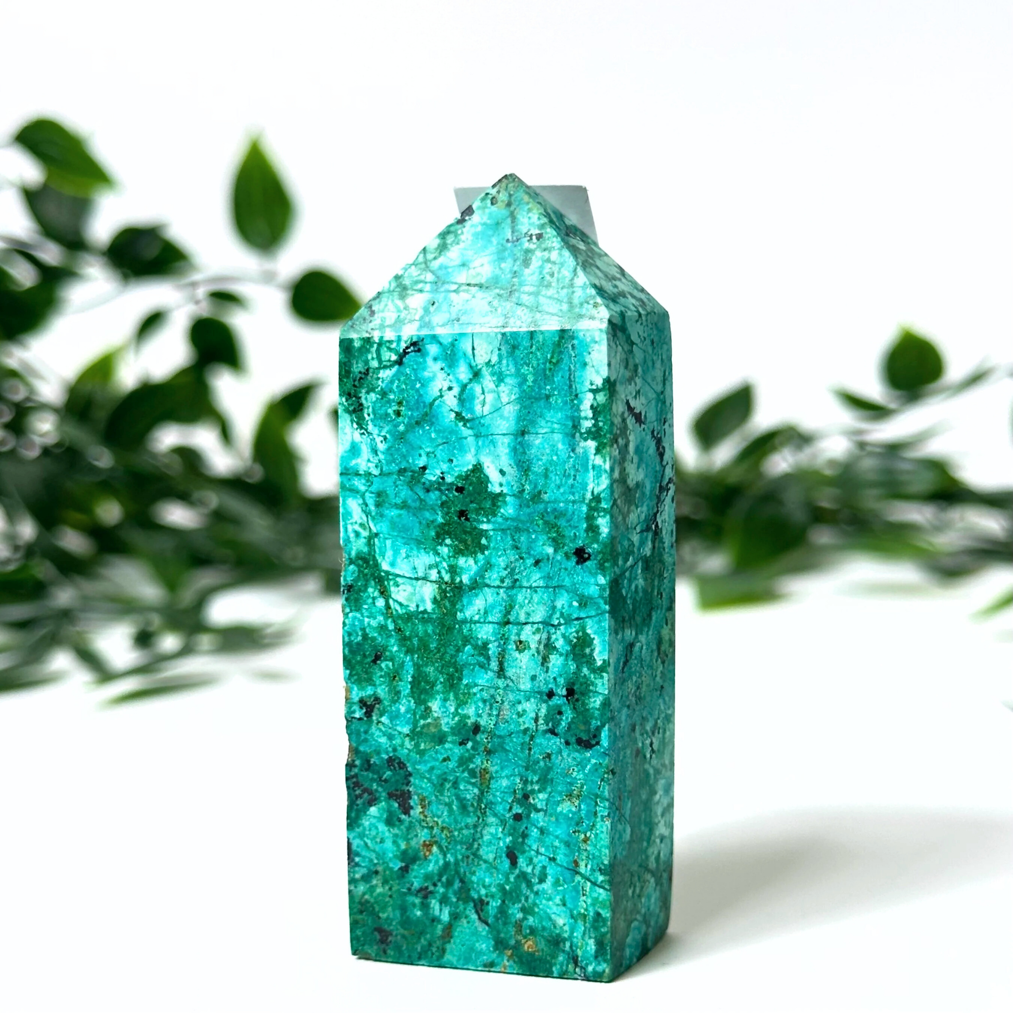 Chrysocolla crystal tower with green leaves in the background