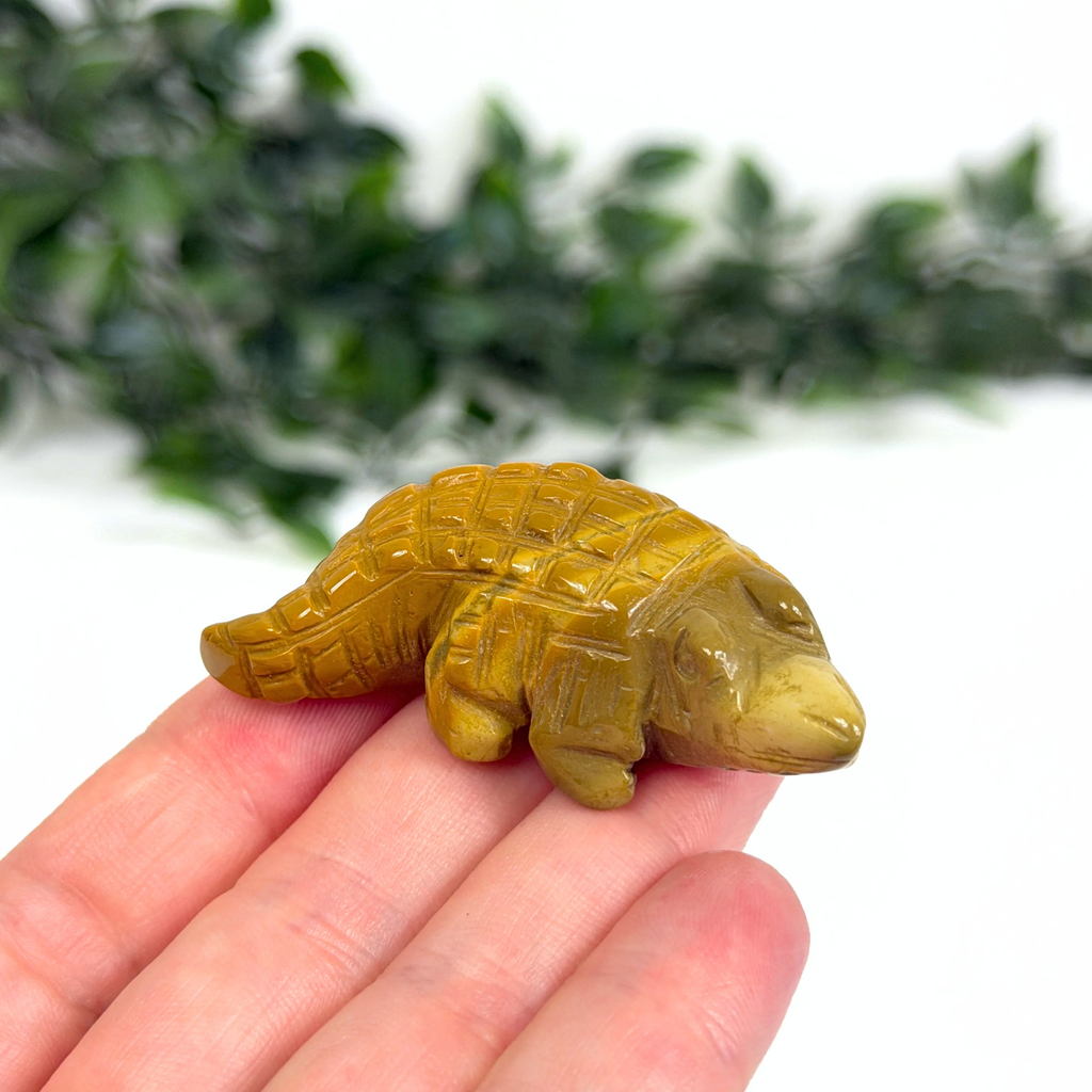 Mookaite crocodile carving held in a hand with a blurred green background